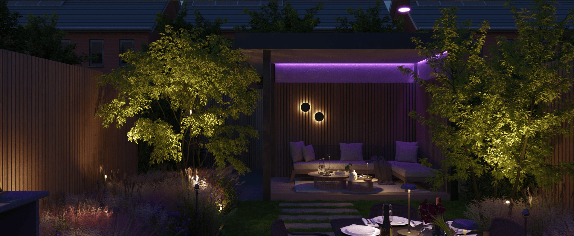 The image depicts a beautifully designed outdoor living space at night. The focal point is a covered seating area with plush, purple-colored sofas and chairs, creating a cozy and inviting atmosphere. This seating area is illuminated by subtle, warm lighting, both overhead and mounted on the surrounding wooden walls. The outdoor space is further enhanced by the presence of a lush, mature tree with vibrant green foliage, which adds a natural and serene element to the scene. A dining table set with dinnerware is also visible, suggesting this area is designed for both relaxation and al fresco dining. The overall impression is one of a well-crafted, harmonious outdoor retreat, perfect for entertaining or enjoying a peaceful evening under the stars.