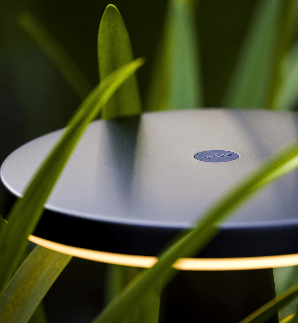 This image showcases a sleek, minimalist design object nestled amidst lush, verdant foliage. The focal point is a round, silver-colored device with a subtle Bose logo, indicating it is likely a Bose audio product. The device is positioned in a way that highlights its elegant, streamlined form, with the surrounding greenery providing a striking contrast and natural backdrop. The lighting in the scene creates a soft, warm glow, adding to the overall sense of tranquility and harmony between the technological device and the natural environment. The composition of the image draws the viewer's attention to the interplay between the man-made object and the organic, living elements of the plants. This juxtaposition suggests a thoughtful integration of design and nature, where the technological product is presented as a complement to, rather than an imposition on, the natural setting. The overall impression is one of a carefully curated and visually striking scene that showcases the design philosophy of the Bose brand, emphasizing the seamless blending of form, function, and environmental context.