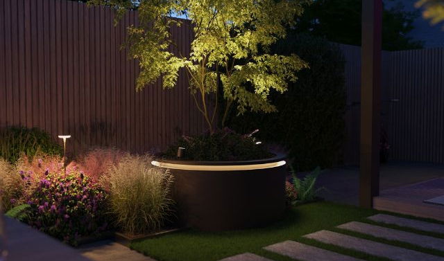 The image depicts a beautifully designed outdoor garden scene at night. The focal point is a large, decorative planter or urn filled with lush, vibrant foliage that is illuminated by strategic landscape lighting, creating a warm and inviting ambiance. Surrounding the planter are carefully placed stepping stones that lead to a covered patio or entryway visible in the background. The garden is further enhanced by the presence of a tall, tree-like plant with brilliant yellow leaves that add a striking contrast to the darker tones of the surrounding plants and hardscaping. The overall impression is one of a thoughtfully curated and meticulously maintained outdoor living space, blending natural elements with contemporary design. The strategic use of lighting, the harmonious integration of plants and materials, and the attention to detail create a visually captivating and serene nighttime garden oasis, inviting the viewer to immerse themselves in the tranquil and inviting atmosphere.